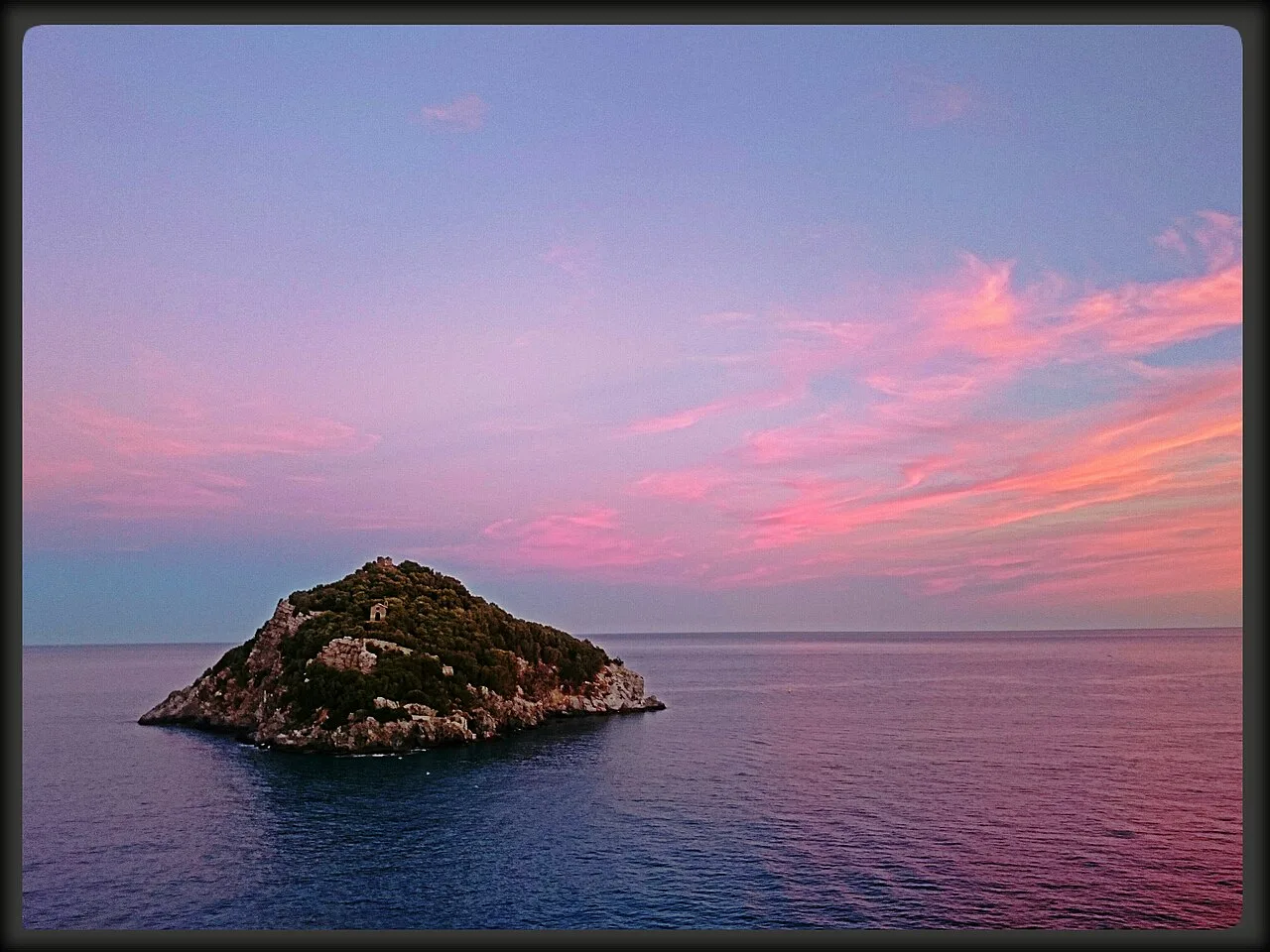 L'Isola di Bergeggi al tramonto in agosto, con il cielo arancione sul golfo