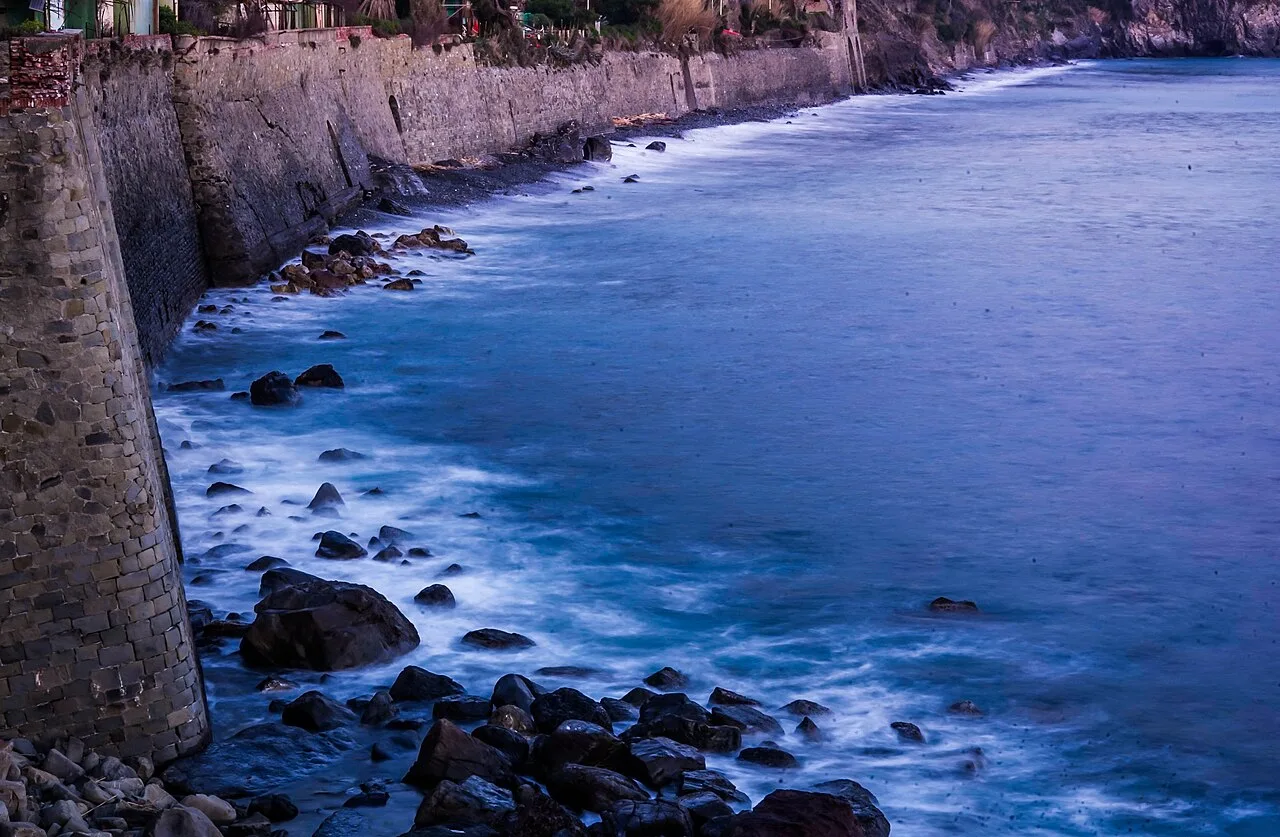 La costa rocciosa di Corniglia vista dal mare: la parete calcarea scende dritta sull'acqua turchese delle Cinque Terre