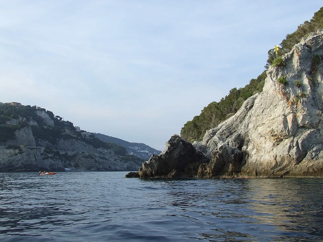Le falesie dell'area marina protetta di Bergeggi viste dal mare, con la croce di Punta Predani e un kayak in acqua