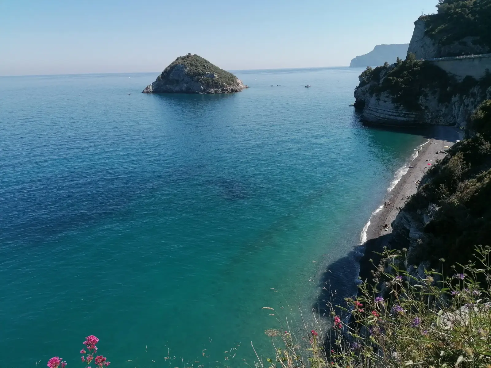 La spiaggia di ciottoli ai piedi del promontorio di Capo Noli, con il mare azzurro e le falesie