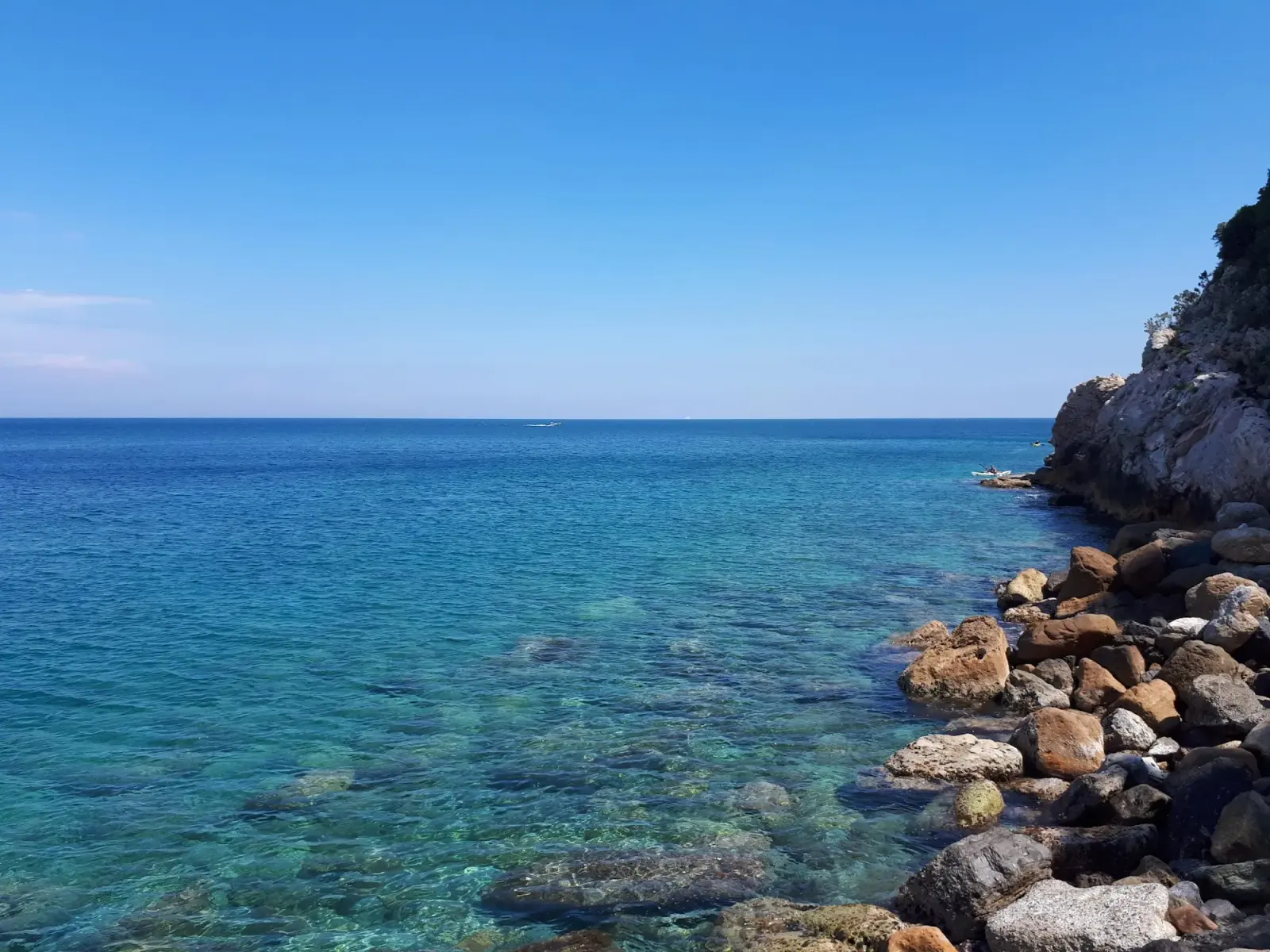 La spiaggia di ciottoli ai piedi del promontorio di Capo Noli, con l'acqua trasparente e le falesie verticali sullo sfondo