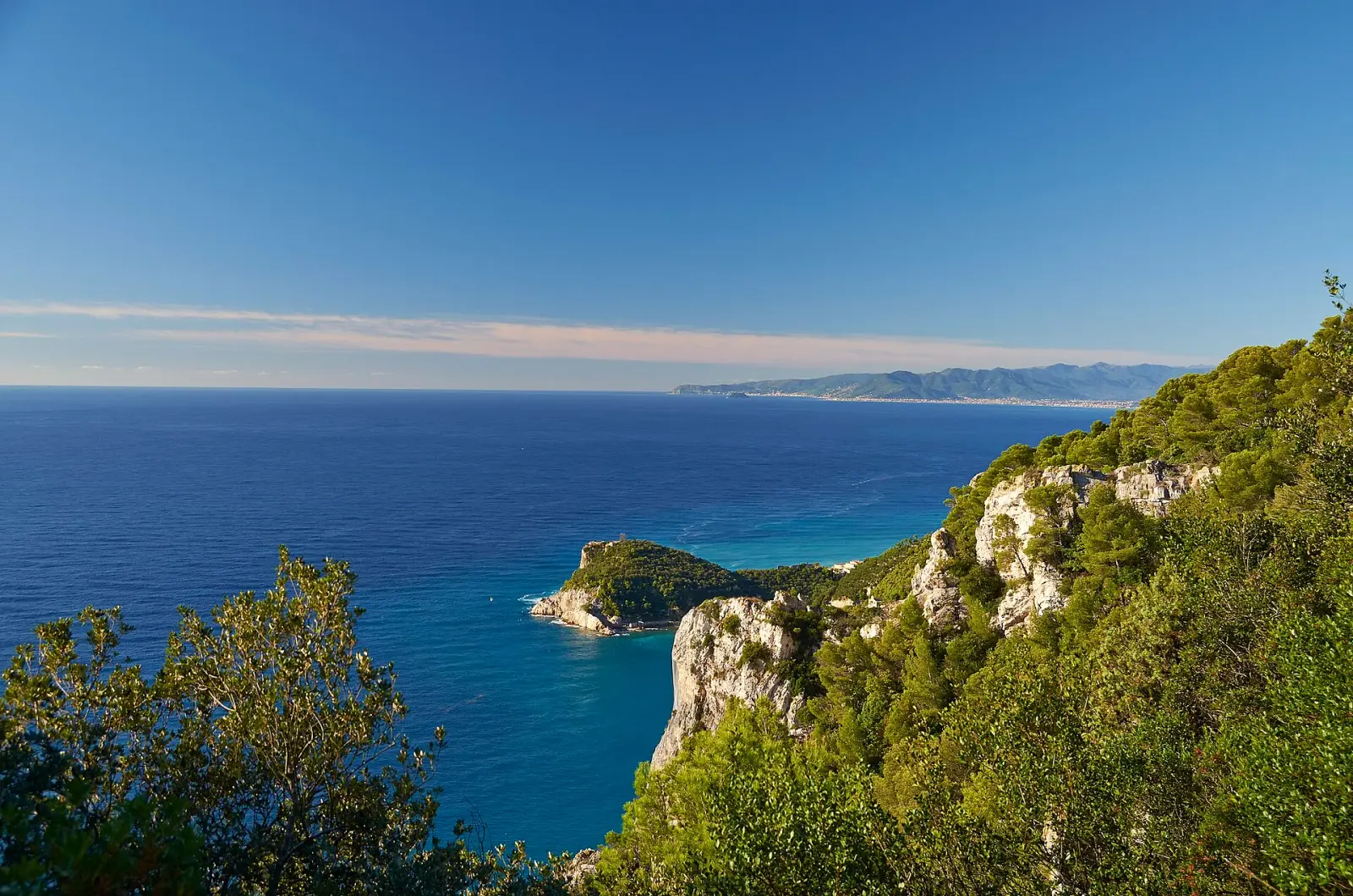 Vista verso il promontorio di Punta Crena dalla costa, con la roccia che scende dritta nel mare e il colore dell'acqua che varia dal verde al turchese